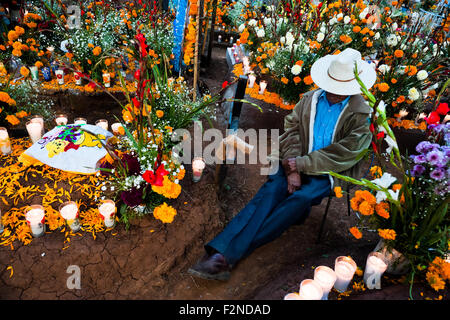 Ein mexikanische Mann sitzt am blumengeschmückten Grab im Laufe des Tages der toten Feier in Tzintzuntzan, Mexiko. Stockfoto