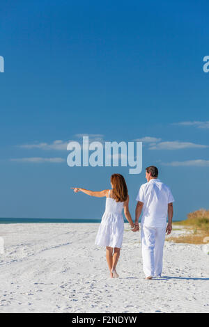 Rückansicht von Mann und Frau romantisch zu zweit in weißen Kleidern gehen Hand in Hand und deutete auf einem einsamen tropischen Strand mit Stockfoto