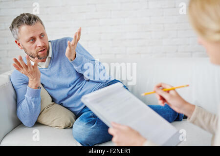 Verwirrten Mann auf Sofa seine Psychologin zu sagen, was passiert ist Stockfoto