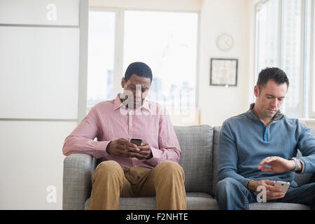 Männer mit Handys warten auf sofa Stockfoto
