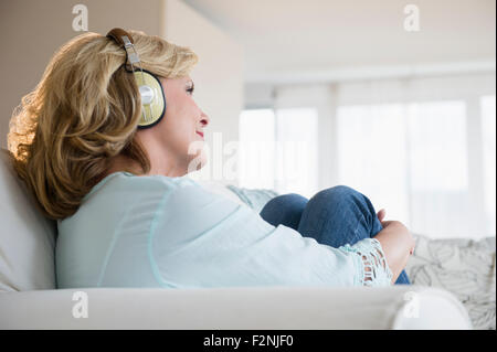 Kaukasische Frau hören Kopfhörer auf sofa Stockfoto