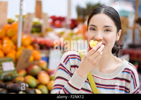 Hispanic Frau essen Obst am Bauernmarkt Stockfoto
