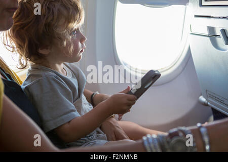 Kaukasische Mutter und Baby Sohn mit Handy im Flugzeug Stockfoto