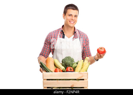 Männliche Jungkoch in weißer Schürze posiert mit einer Kiste voller frisches Gemüse und eine einzelne Tomate in seiner Hand hält Stockfoto