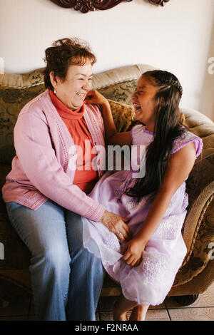 Hispanische Großmutter und Enkelin lachend auf sofa Stockfoto