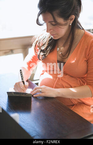 Schwangere Frau schreiben Karte am Tisch Stockfoto