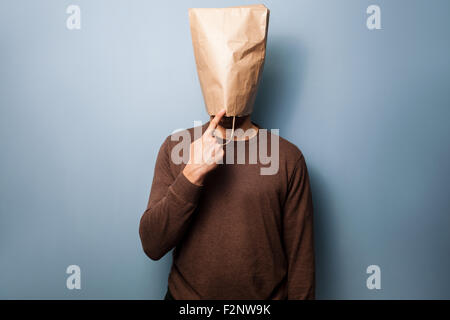 ein junger Mann mit einer Papiertüte auf dem Kopf ist nachdenklich in Richtung Kinn zeigen. Stockfoto