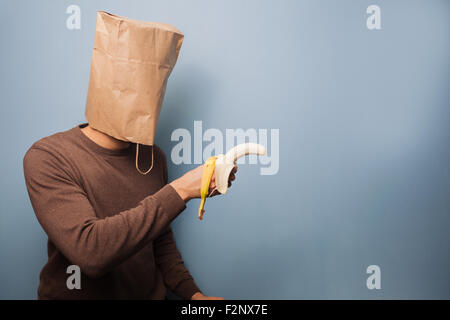 ein junger Mann mit einer Papiertüte auf dem Kopf zeigt eine Banane, als wäre es eine Waffe! Stockfoto