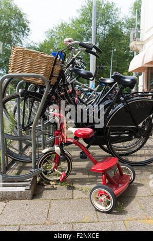 AMSTERDAM - 2. August 2015: Kleine rote Dreirad auf einem Bürgersteig geparkt. In Amsterdam gibt es so viele Fahrräder wie gibt es resi Stockfoto