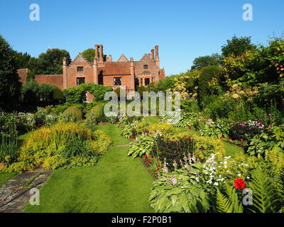 Chenies Manor House und versunkene Garten mit schönen mehrjährige Blumenrabatten, Pfad und frischem grünem Laub; sonnig mit blauem Himmel. Stockfoto
