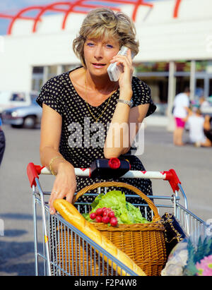 Reife Frau sprechen über ihr Mobiltelefon während des Einkaufs im Supermarkt Stockfoto