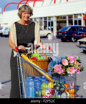 Reife Frau beim Einkaufen mit Blick auf die Kamera, lächelnd reife Frau mit Einkaufswagen auf dem Supermarkt-Parkplatz, Frankreich, Europa Stockfoto