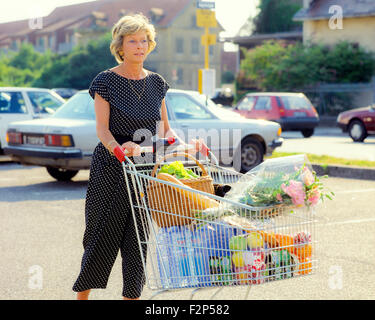 Reife Frau mit Einkaufswagen im Supermarkt-Parkplatz, Stockfoto