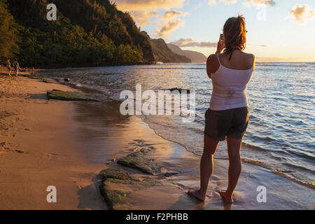 Tourist bei Kee Beach bei Sonnenuntergang nimmt ein Foto von der Na Pali Küste Stockfoto