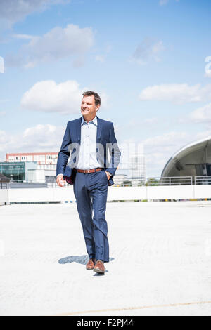 Geschäftsmann im Anzug zu Fuß auf Parkdeck, Lächeln Stockfoto