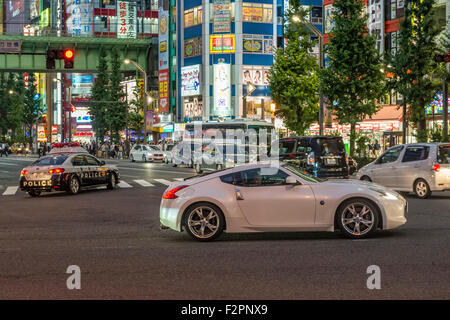 Ein schnelle Sportwagen wartet wieder mit einem Polizeiwagen im Hintergrund in Akihabara Stockfoto