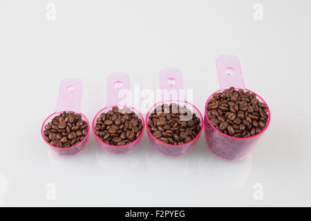Kaffeebohnen im Messbecher in verschiedenen Größen auf weiß. Stockfoto