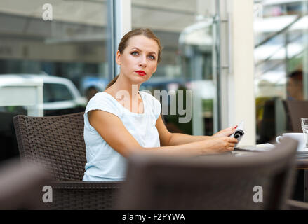Attraktive junge Frau mit roten Lippen liest eine Zeitung, die sitzen in einem café Stockfoto