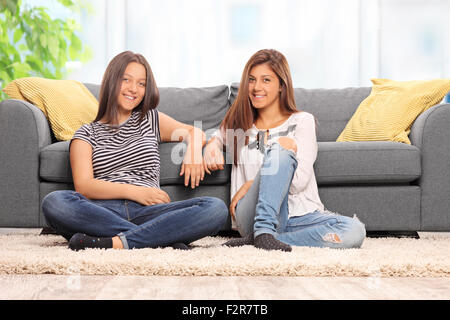 Zwei glückliche Mädchen sitzen auf dem Boden vor einem modernen grauen Sofa zu Hause Stockfoto