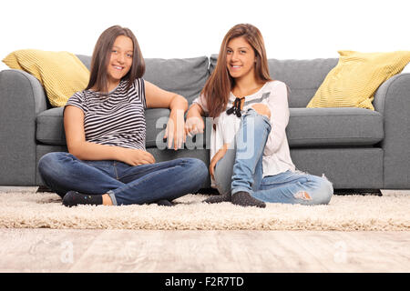 Zwei Mädchen im Teenageralter vor einem grauen Sofa sitzen und mit Blick auf die Kamera auf weißem Hintergrund isoliert Stockfoto