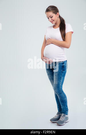 Voller Länge Porträt einer schwangeren Frau streichelt ihren Bauch isoliert auf weißem Hintergrund Stockfoto