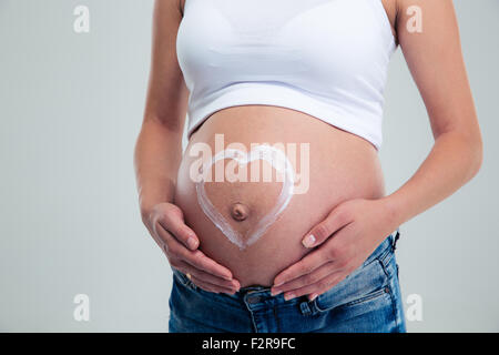 Schwangere Frau mit Herzform auf Bauch aus Sahne hergestellt Stockfoto