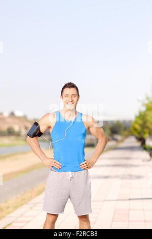 Vertikale Schuss eines jungen männlichen Athleten anhören von Musik auf seinem Handy und stehen auf einem Bürgersteig Stockfoto
