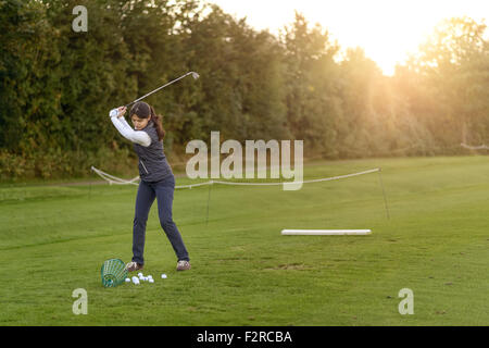 Golfspielerin stehend auf der driving Range am späten Nachmittag am Tag, während des Swingens konzentrieren ihr club Stockfoto