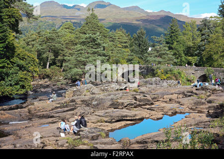 Menschen entspannen auf den Felsen rund um Stürze Dochart bei Killin, Schottland mit dem Tarmachan Grat im Hintergrund. Stockfoto