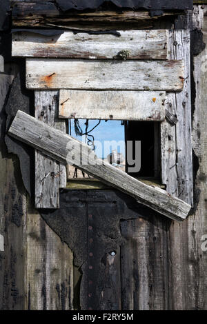 Aufgegeben, Angelboot/Fischerboot gesehen durch das verschalten Fenster von einem alten Fischer Schuppen, Dungeness, Kent, England, UK Stockfoto