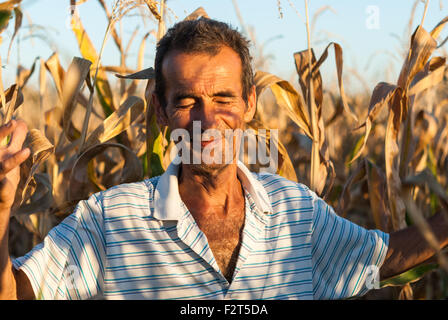 Outdoor Portrait des rumänischen Bauern glücklich und lächelnd in die Mais-Feld-Nahaufnahme bei Sonnenuntergang. Stockfoto
