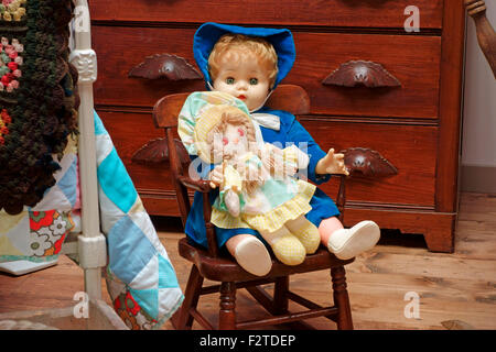 Puppen auf einem Schaukelstuhl neben einem Bett in einem Kinderzimmer Stockfoto