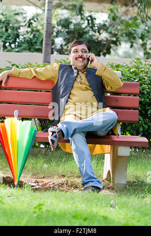 1 indische erwachsenen Mannes sitzen Parkbank Handy im Gespräch Stockfoto