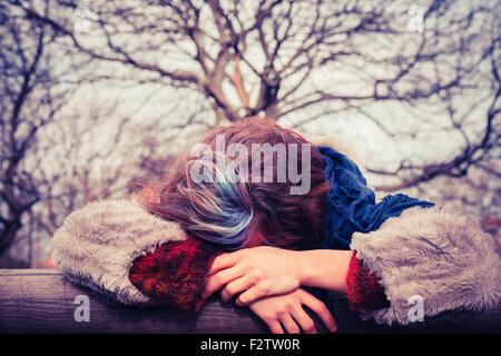 Eine junge Frau lehnt an einem Holzbalken im park Stockfoto