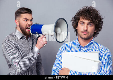Wütend Geschäftsmann schreien über Megaphon mit einem anderen Mann über grauen Hintergrund Stockfoto