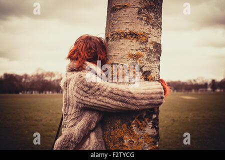 Junge Frau im Park an einem Wintertag und umarmt einen Baum Stockfoto
