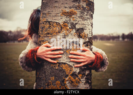 Junge Frau im Park an einem Wintertag und umarmt einen Baum Stockfoto