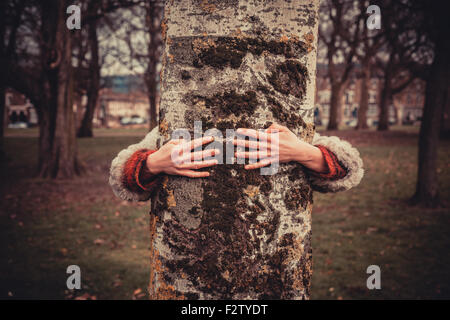 Junge Frau im Park an einem Wintertag und umarmt einen Baum Stockfoto