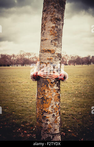 Junge Frau im Park an einem Wintertag und umarmt einen Baum Stockfoto