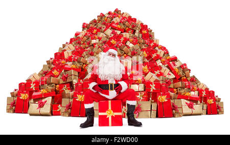 Weihnachtsmann sitzt vor einem Haufen von Weihnachtsgeschenken isoliert auf weißem Hintergrund Stockfoto