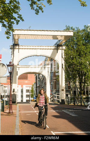 Ein Mann auf einem Fahrrad über eine hölzerne Brücke über den Fluss Amstel, Amsterdam Stockfoto