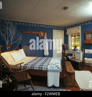 Blau + weiß aufgegebenes Decke auf dem Bett mit gedrehten Spindeln im blauen Schlafzimmer mit antiker Holzstuhl Stockfoto