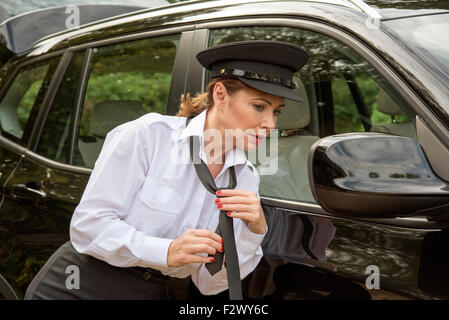 Attraktive Frau Chauffeur binden ihre uniform Krawatte in den Außenspiegel ihres Autos Stockfoto