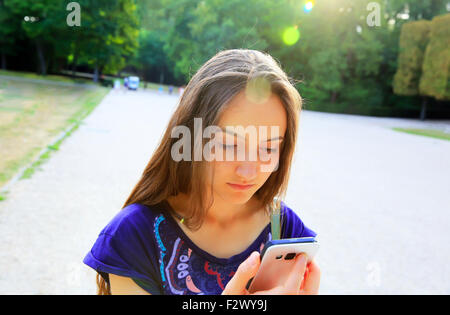 Mädchen mit einem Mobiltelefon liest die Nachricht im park Stockfoto