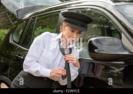 Attraktive Frau Chauffeur binden ihre uniform Krawatte in den Außenspiegel ihres Autos Stockfoto