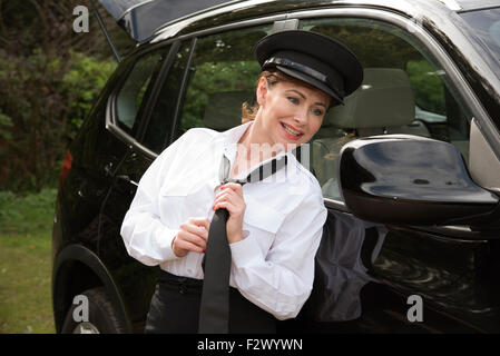 Attraktive Frau Chauffeur binden ihre uniform Krawatte in den Außenspiegel ihres Autos Stockfoto