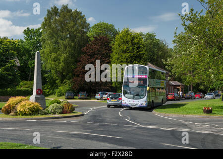 Dorf Datenverkehr einen Steinen Obelisk (WW1 Kriegerdenkmal mit Mohn Kranz) auf einem kleinen Kreisverkehr in sonnigen oberen Poppleton, in der Nähe von York, England, UK. Stockfoto