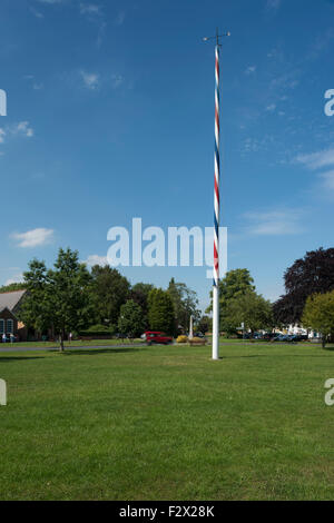 Groß, rot, weiß und blau gestreifte Maibaum auf dem schönen Dorfplatz des oberen Poppleton (in der Nähe von York, England, UK) gegen einen blauen Sommerhimmel. Stockfoto