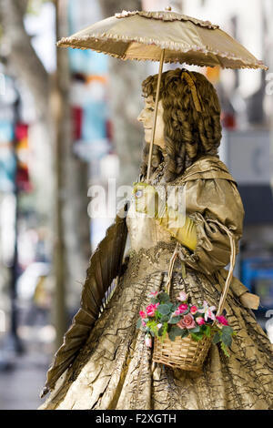 Frau in Gold mit Korb mit Blumen als Straßenmusikant auf der Straße von Barcelona Stockfoto