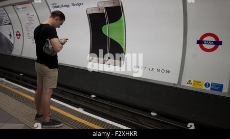 Männlichen Blick auf Handy vor Werbung Horten Plakat am Londoner u-Bahn Anzeigen Samsung Galaxy S6 Kante Stockfoto